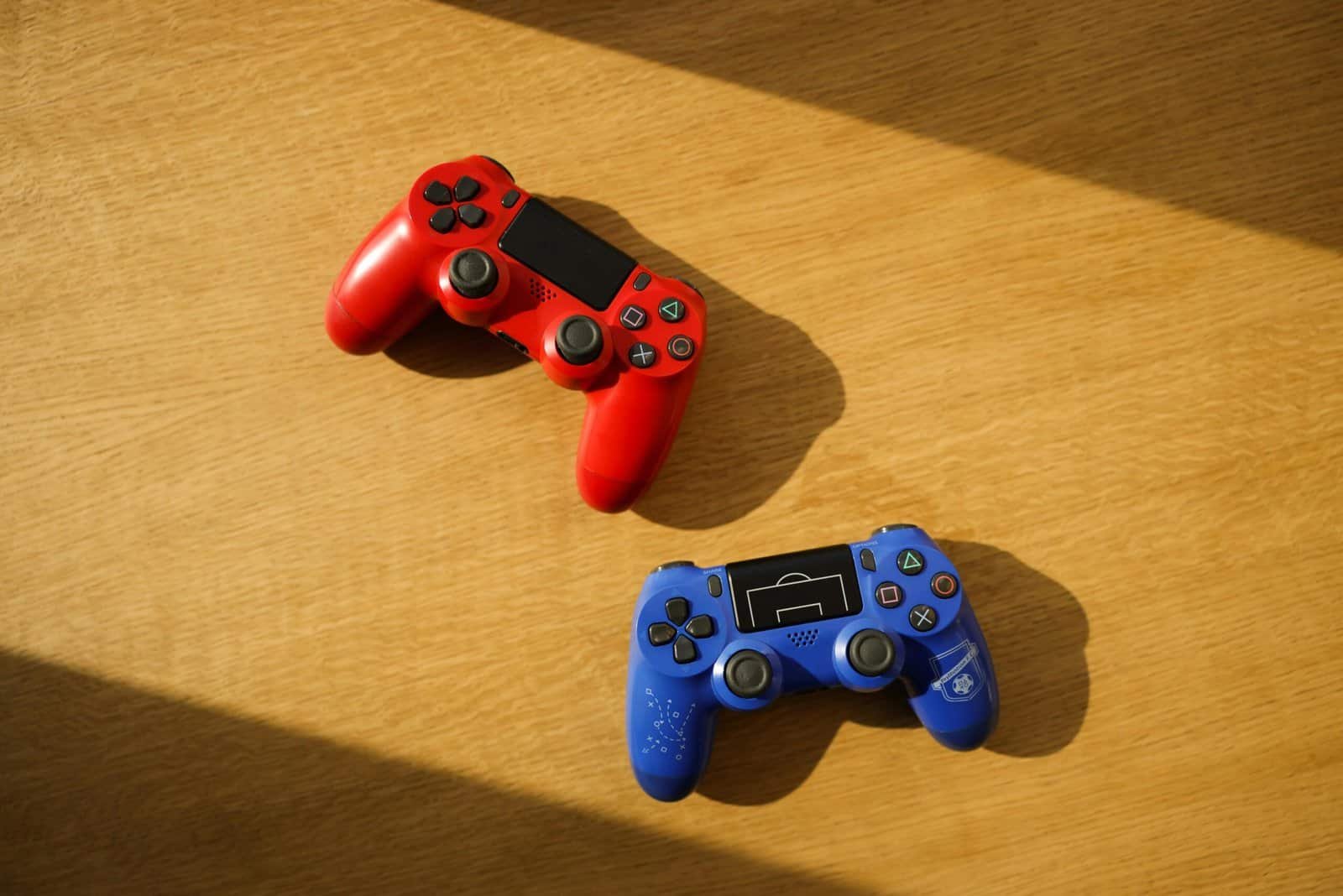 Two colorful gaming controllers placed on a wooden surface with sunlight casting shadows.